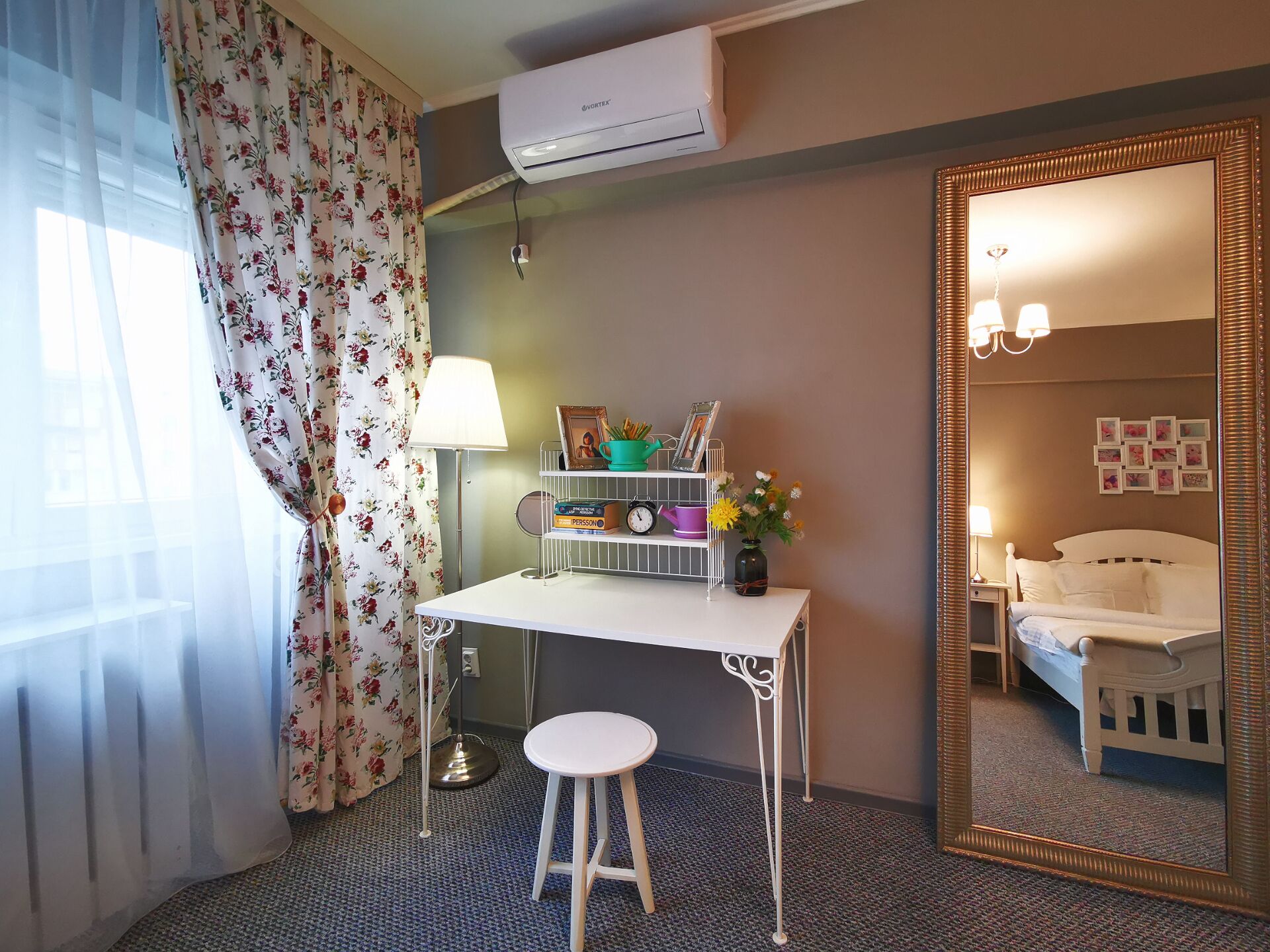 Ett hotellrum med ett skrivbord, en stol, en spegel, en säng och ett fönster med gardiner.