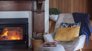 Un salon chaleureux avec une cheminée, un fauteuil confortable avec des coussins, une petite table et un panier.