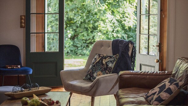 Un salon chaleureux avec un canapé en cuir, un fauteuil à capitons et une table basse en bois sur laquelle sont disposés des fruits.
