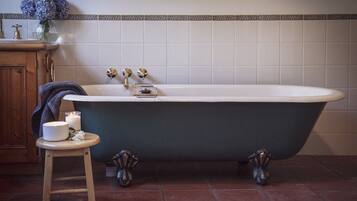 A bathroom with a freestanding bathtub, a wooden cabinet, a small stool with a candle and a flower, and a vase with blue flowers on the counter.
