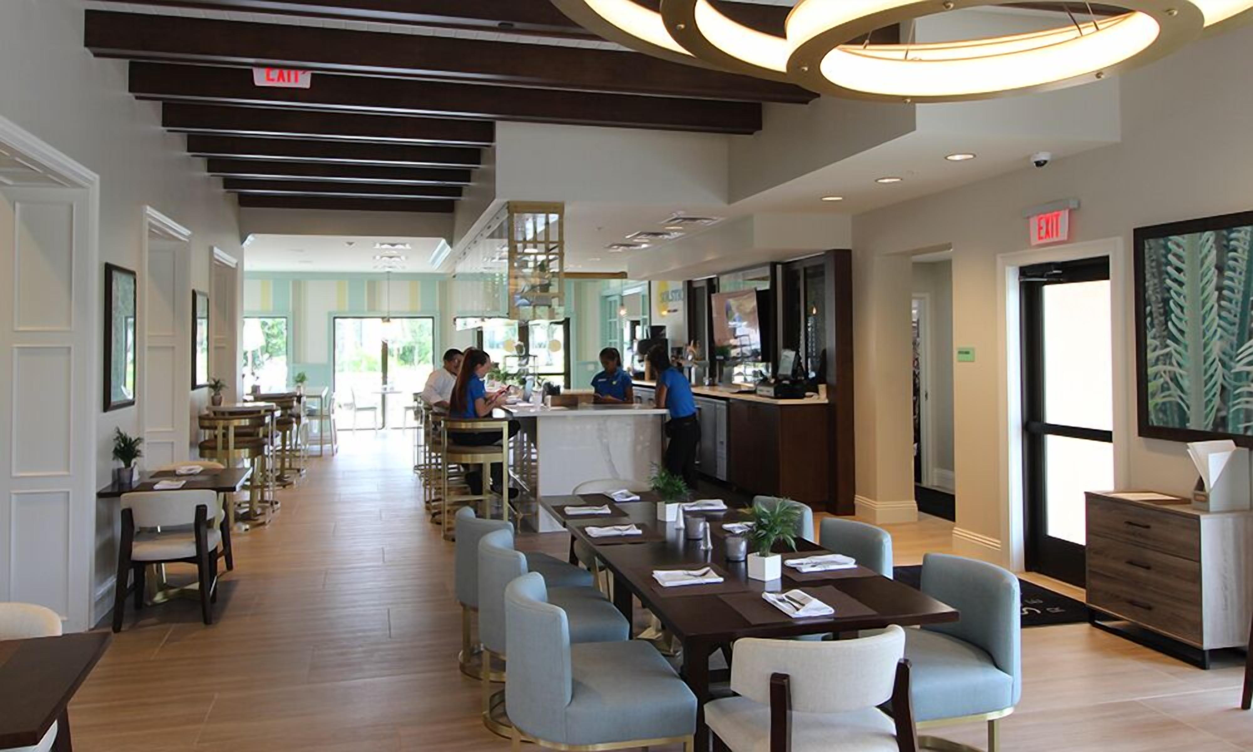 Een ruim restaurant met hoge plafonds, moderne verlichting en een mix aan zitmogelijkheden, waaronder tafels en barstoelen.