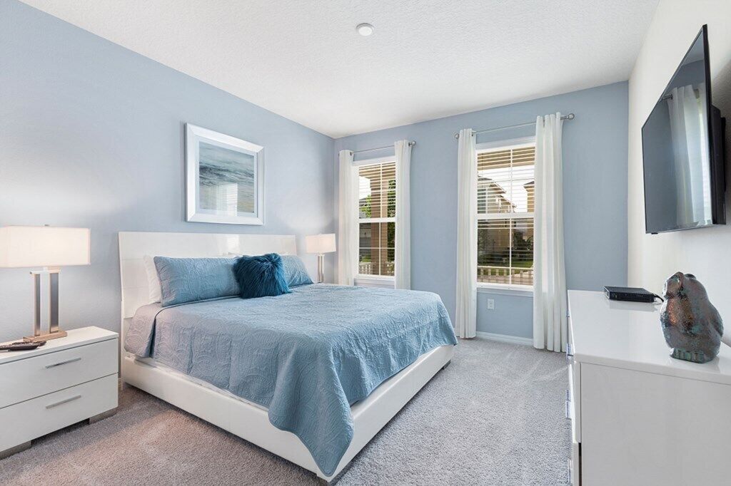 A bedroom with a bed, a nightstand, a dresser, a flat-screen TV, and a window with curtains.