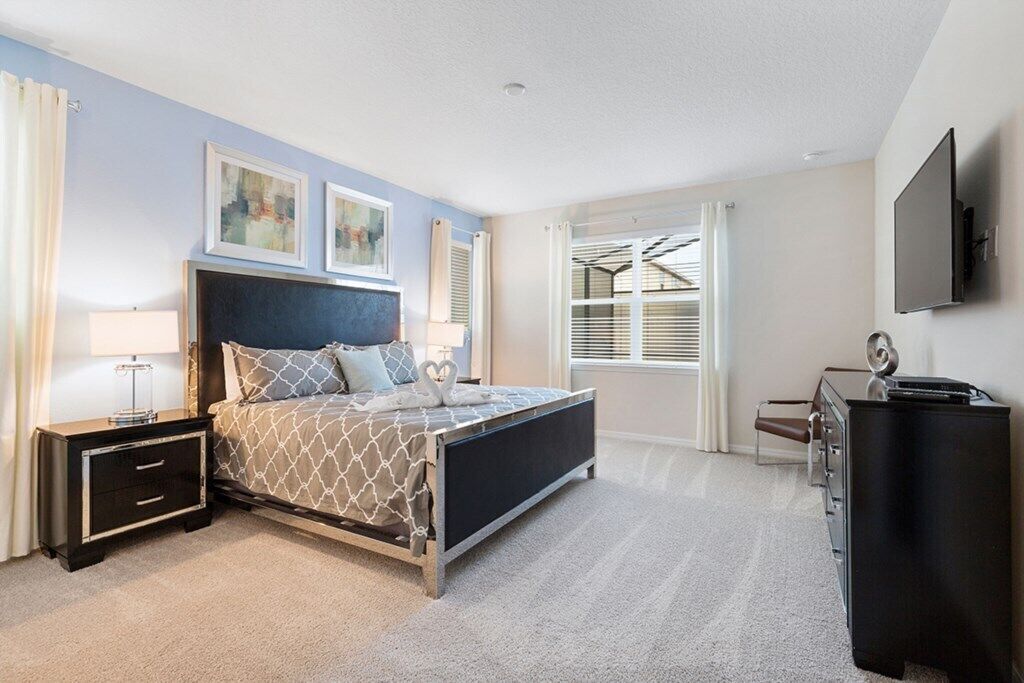 A bedroom with a bed, bedside tables, a dresser, and a TV mounted on the wall.