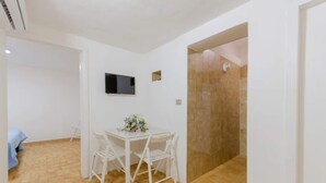 A small room with a white table and chairs, a flat-screen TV mounted on the wall, and a shower area with tiled walls. - Miramare House - Trilo 4 C (Mattinata)