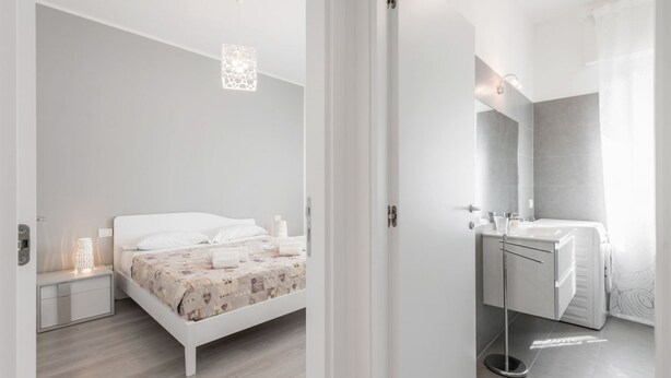 Un dormitori modern amb un llit, una taula de nit i un bany amb un lavabo i un mirall.