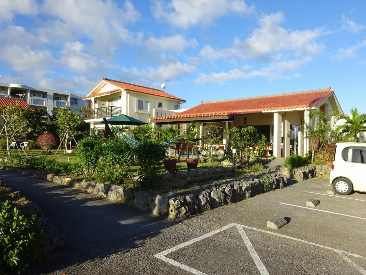 A parking area with a building featuring a red-tiled roof and a covered outdoor seating area.