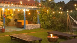 Un espace extérieur aménagé en terrasse, avec des guirlandes lumineuses, des tables en bois et un foyer.