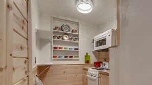 A compact kitchen with wooden cabinetry, a microwave, a stove, and a shelf with colorful bowls. - ~New~ Yellowstone Rock Studio (Gardiner)