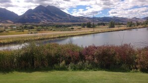 A river with mountains in the background, a grassy area in the foreground, and a clear sky. - ~New~ Yellowstone Rock Studio (Gardiner)