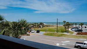 Una strada costiera con auto parcheggiate, vista libera sulla spiaggia e un parcheggio con segnale di limite di velocità.
