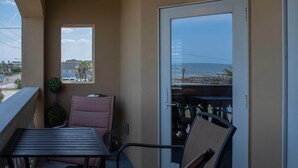Un balcone con tavolo e sedie, una pianta in vaso, e vista sulla spiaggia e sull'oceano.