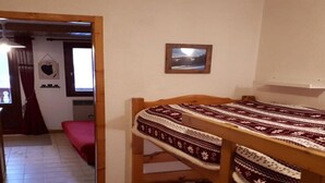 A bunk bed with a patterned bedspread, a small framed picture on the wall, and a window with curtains. - Cozy studio in Champagny, for 4 guests, south-facing balcony (Champagny-en-Vanoise)