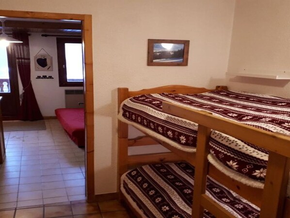 A bunk bed with a patterned bedspread, a small framed picture on the wall, and a window with curtains. - Cozy studio in Champagny, for 4 guests, south-facing balcony (Champagny-en-Vanoise)