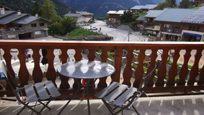 A balcony with a table and chairs overlooking a mountain village with traditional buildings and a road. - Cozy studio in Champagny, for 4 guests, south-facing balcony (Champagny-en-Vanoise)