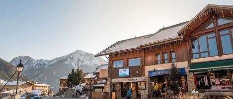 A mountain town with a stone building labeled "OFFICE DE TOURISME" and a shop named "MGM CONSTRUCTION".