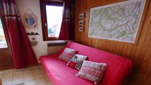 A cozy room with a red sofa, a large map on the wall, and a window with curtains. - Cozy studio in Champagny, for 4 guests, south-facing balcony (Champagny-en-Vanoise)