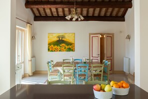 A dining area with a wooden table, blue chairs, and a painting of a tree on the wall.
