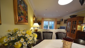 Un coin repas avec une table dressée pour deux personnes, un vase rempli de fleurs jaunes et un buffet en bois aux portes vitrées.