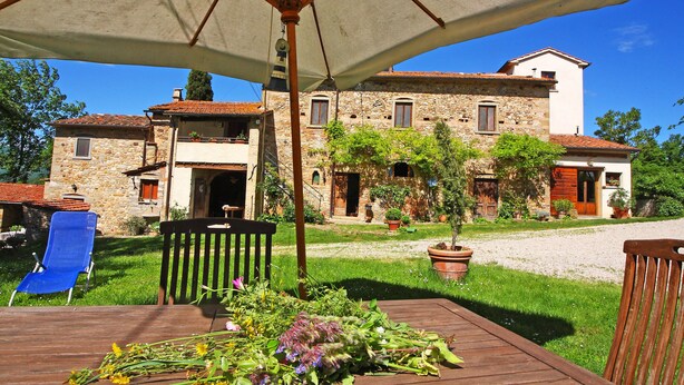 A stone building with a tiled roof, a wooden bench, and a table with flowers. - Farmhouse in the Tuscan countryside (Anghiari - Arezzo)