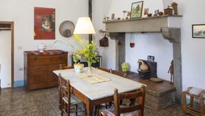 A dining area with a marble table, wooden chairs, a vase with flowers, a wooden cabinet, and a fireplace with various decorations. - Farmhouse in the Tuscan countryside (Anghiari - Arezzo)