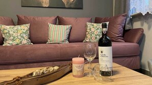 Un salon chaleureux avec un canapé, des coussins décoratifs, une bouteille de vin, une bougie et un verre posés sur une table en bois.