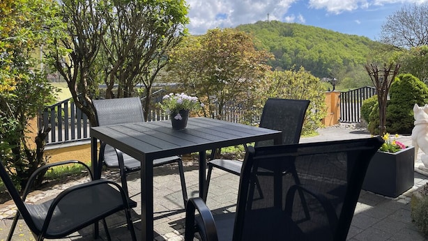 Une terrasse extérieure avec une table et des chaises, entourée d’arbres et offrant une vue sur une colline.