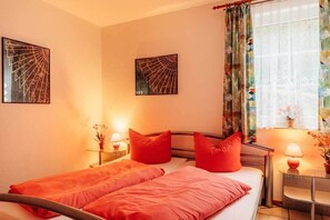 A bedroom with two beds, red bedding, and two wall-mounted artworks.