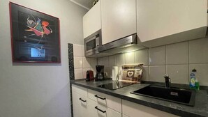 Une cuisine moderne avec des armoires blanches, un comptoir noir, un four à micro-ondes encastré et une hotte de cuisinière en acier inoxydable.