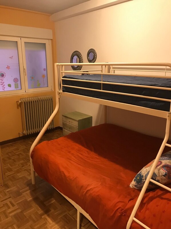 A bunk bed with a red mattress, a radiator, a window with floral decals, and a small dresser. - QUEVEDO PLAZA BIERZO (León)