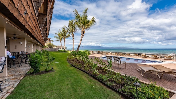 A poolside area with a view of the ocean, palm trees, and a grassy lawn.