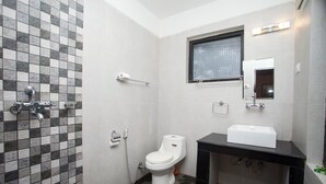 Et badeværelse med flisebeklædt brusevæg, toilet, håndvask og et vindue.