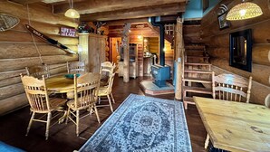 A log cabin interior with a dining area, kitchen, and a staircase.