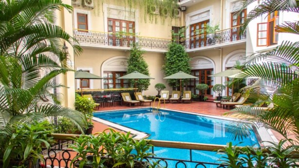 Hotel de varios niveles con piscina central, balcones y abundante vegetación.
