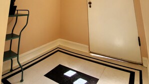 Een kamer met een witte deur, een klein raam en een zwart-wit patroon op de vloer.