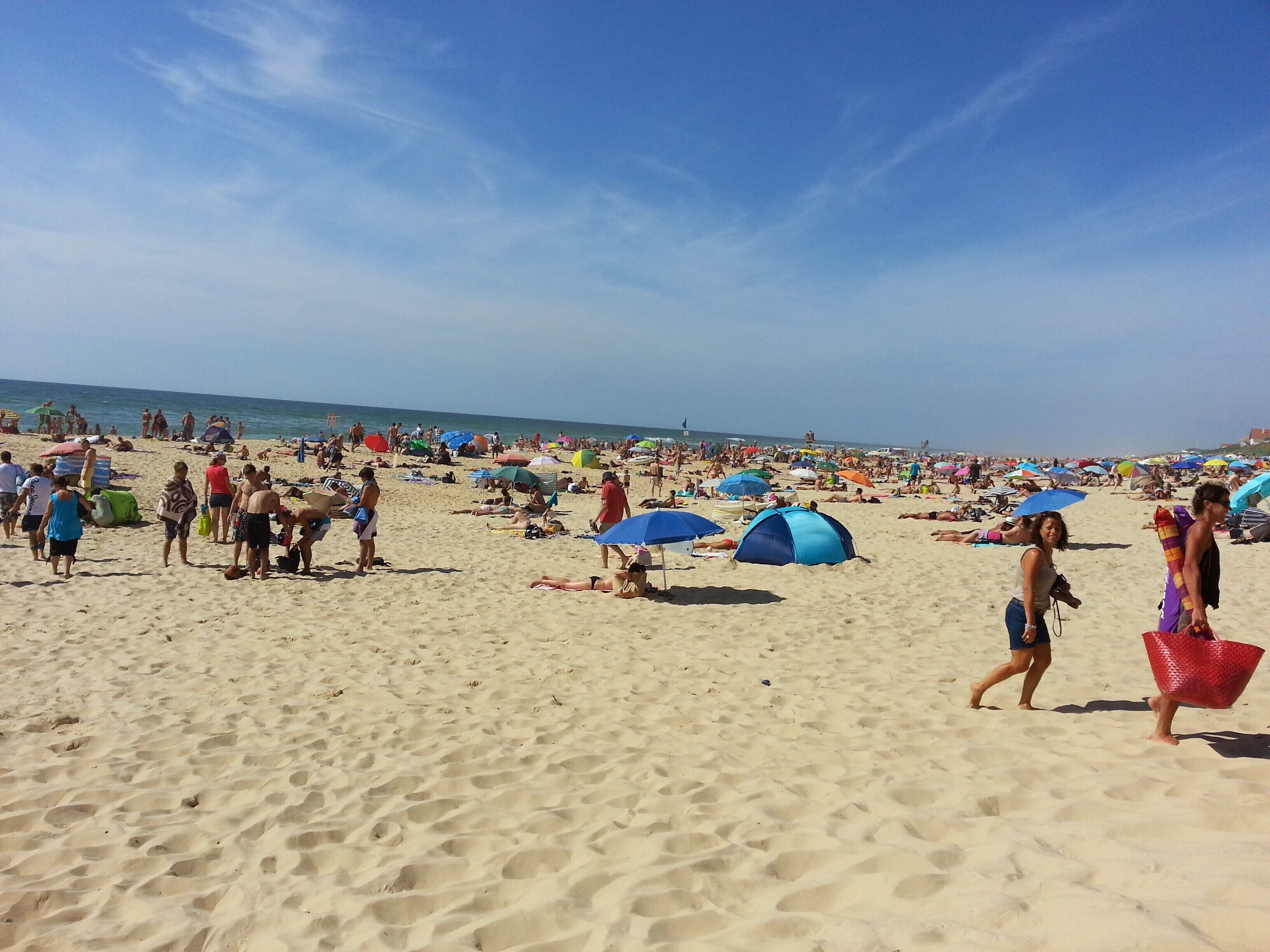 Una spiaggia affollata con persone che prendono il sole e passeggiano.