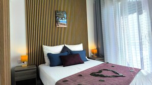 A neatly made bed with a white comforter and multiple pillows, a wooden slat wall panel, a small bedside table with a lamp, and sheer curtains on a window. - BEAUTIFUL APARTMENT 400 M FROM THE BEACHES OF MIMIZAN WITH INTERNET  (Mimizan)