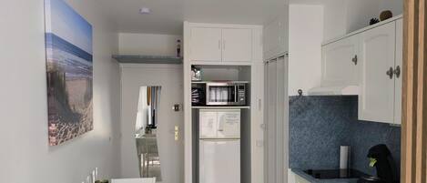 A compact kitchen with white cabinets, a microwave, a refrigerator, and a dining area with a table and chairs.
