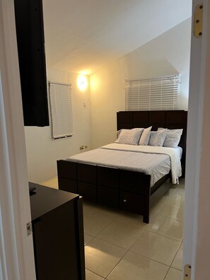 A bedroom with a bed, bedside tables, a desk, and a window with blinds.