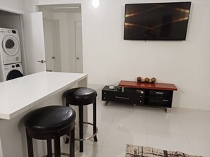 A modern kitchen with a white countertop, two black stools, a wooden cabinet, and a television on the wall.