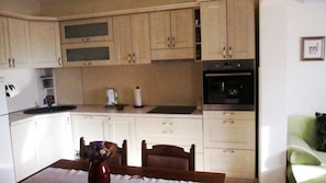 A compact kitchen with white cabinets, a black oven, and a dining table with chairs.