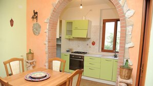 A compact kitchen with green cabinets, a dining table with chairs, and a stone wall archway.