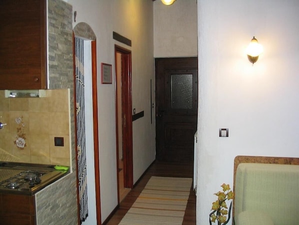 A hallway with a kitchen area on the left, a door with a window, and a chair on the right.