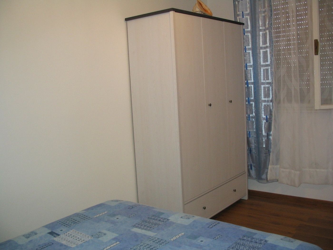 Une chambre à coucher avec un lit, une armoire et une fenêtre avec des rideaux.