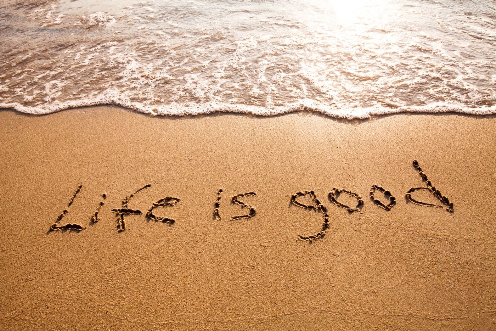 A beach with the words "Life is good" written in the sand.