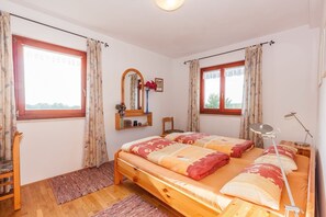 Une chambre avec deux lits, une tête de lit en bois, une table de chevet avec une lampe, un miroir et une fenêtre avec des rideaux.