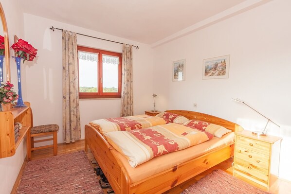 Une chambre à coucher avec un lit en bois, une table de chevet, une commode, une chaise, un bureau avec un miroir et une fenêtre avec des rideaux.