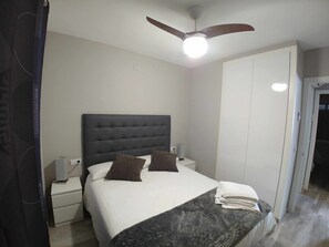 Quarto com cama grande, ventilador de teto, mesa de cabeceira e guarda-roupa.