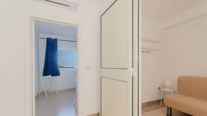 A room with a sliding door, a beige sofa, a small white table with a lamp, and a blue curtain in the doorway. - Miramare House - Trilo 4 B (Mattinata)