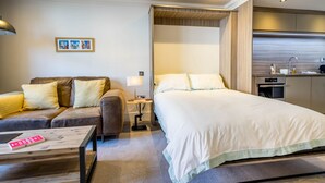 A modern hotel room with a sofa, a bed, a small table, and a kitchenette.