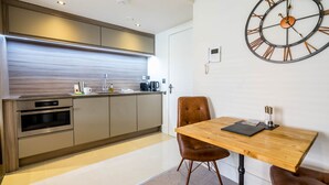 A modern kitchen with stainless steel appliances, a wooden dining table, and a large wall clock.